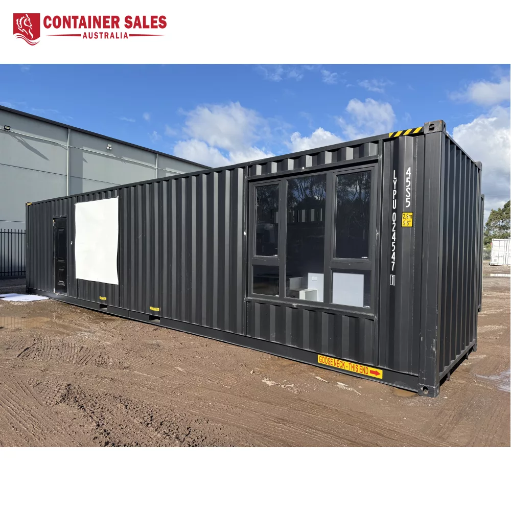 40ft High Cube Accommodation Container Home 1 Dark gray shipping container converted into an office with large glass windows and a door on a dirt lot under a blue sky.