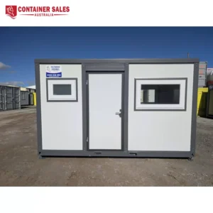 Portable office container with a central door and two rectangular windows, gray trim, on a dirt lot under a blue sky.