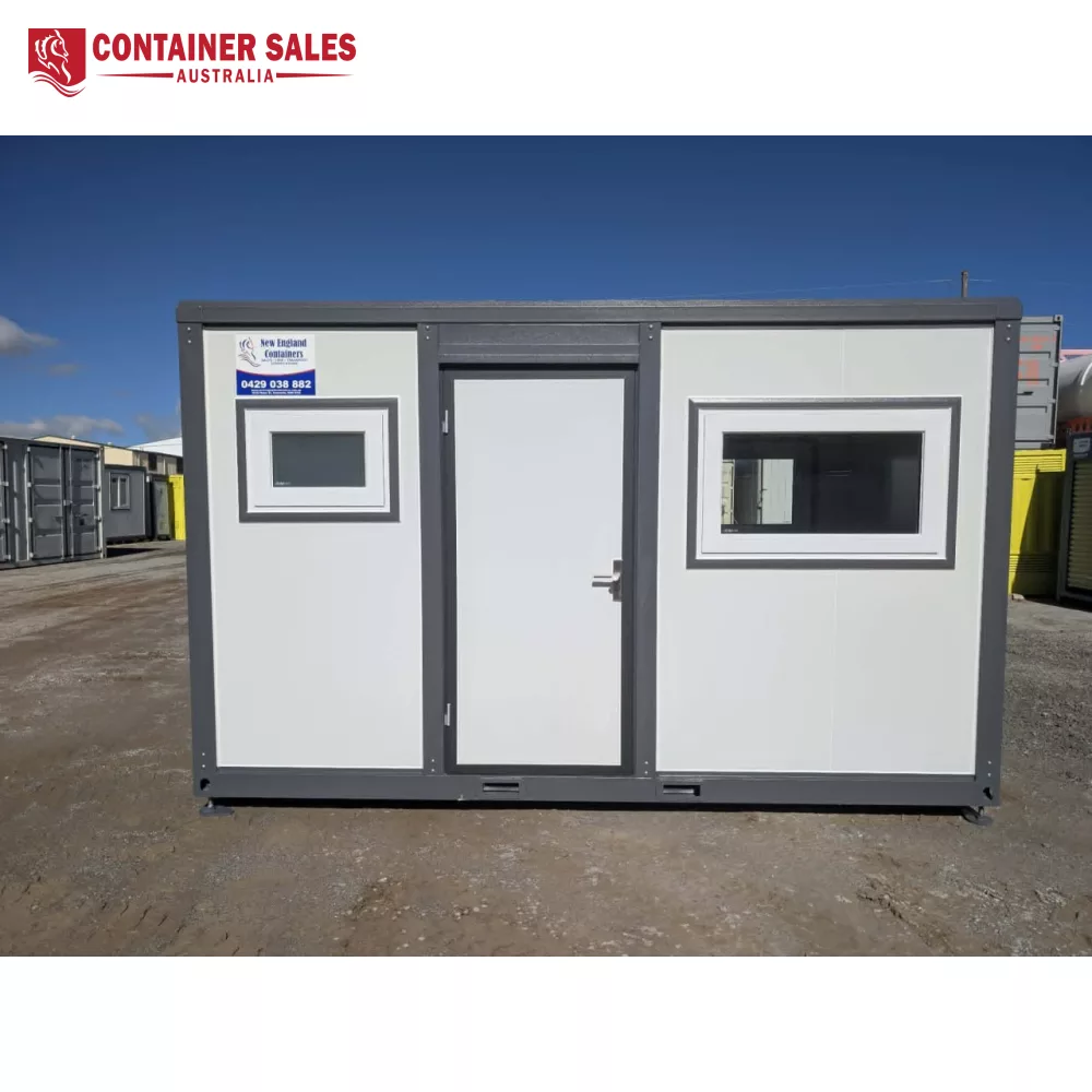 4m Accommodation Unit (Box) – Portable Cabin 1 Portable office container with a central door and two rectangular windows, gray trim, on a dirt lot under a blue sky.