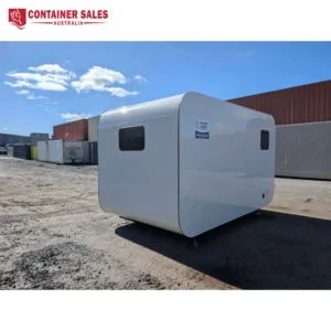 White rounded portable modular cabin in an industrial yard, with shipping containers and a blue sky.