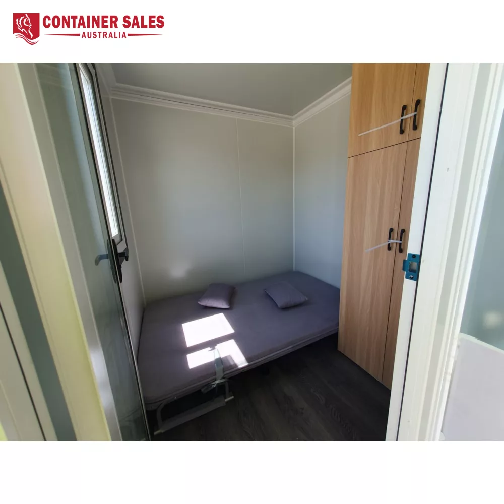 6m 2-Room Accommodation Unit (Type C) 3 Small bedroom in a container with a single bed, two gray pillows, gray walls, and a tall wooden wardrobe by the door.